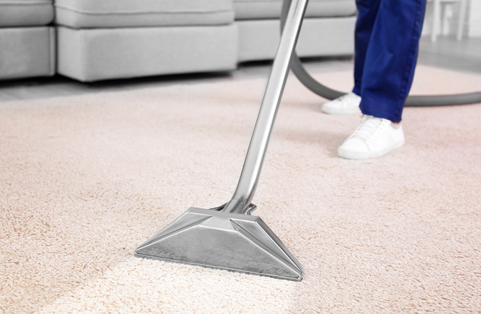 A man is cleaning carpet with vacuuming cleaner